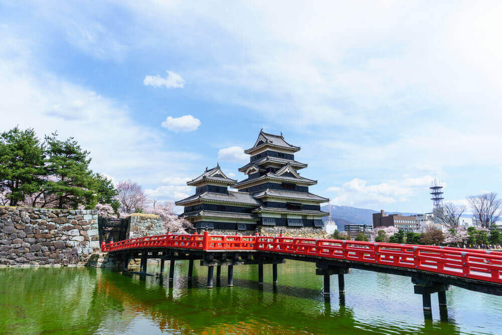 landscape view of Matsumoto Castle and red wooden bridge against blue sky and cloud. this castle symbol of japan ancient feudal historic culture in Nagano,Japan. touring plans