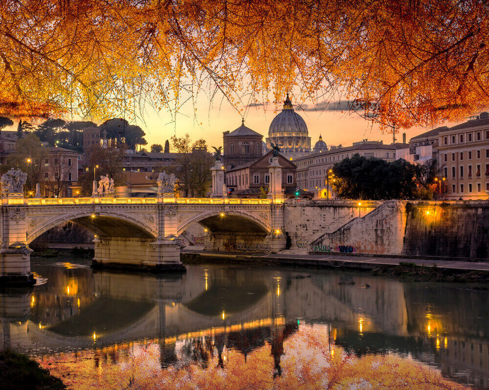 Rome and Vatican, cityscape at sunset with yellow, golden and orange autumn leaves, with St peter's basilica and bridge over the river Tiber. Italy in September