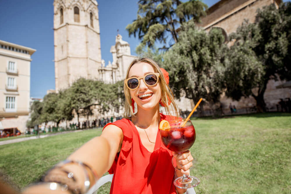 travel to europe. Young woman making selfie photo with sangria, traditional spanish alcohol drink, sitting outdoors in the old town of Valencia