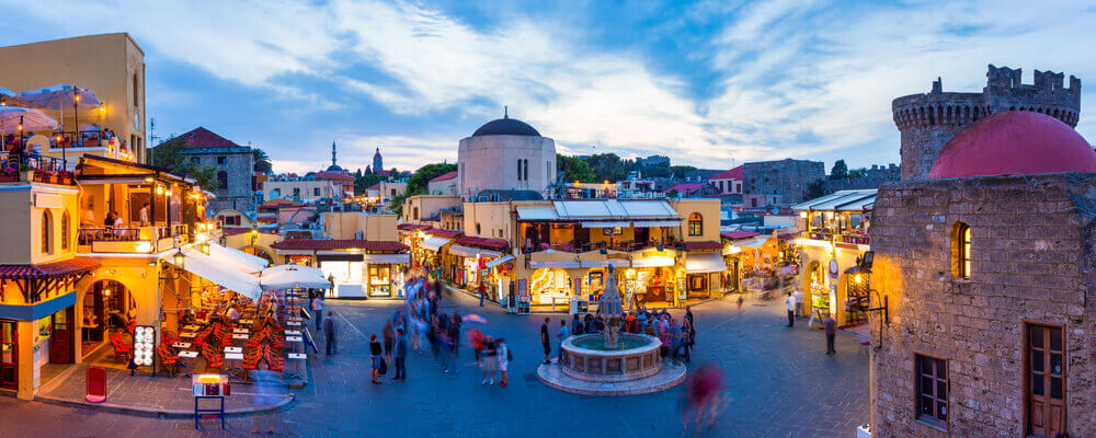 Twilight view of fountain and surrounding cafes in the old town of Rhodes. online trip planner.
