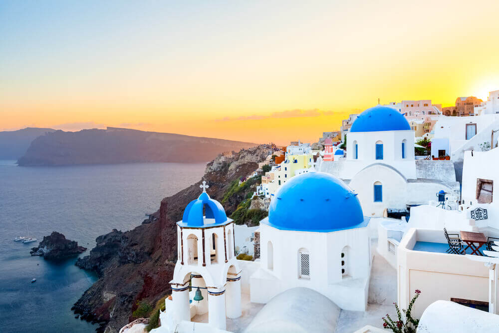 Sunset view of white buildings with blur domes in Oia, Santorini. online trip planner.